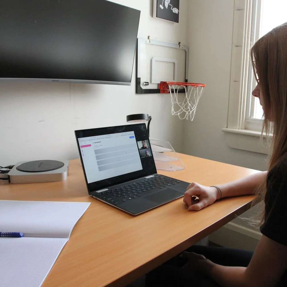 Student at her desk during an online lesson, her notebook open beside the laptop