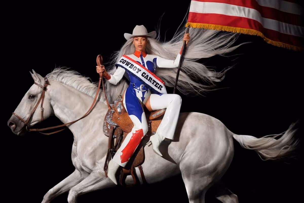Beyoncé sitting on a horse, facing the viewer. She holds an American flag.