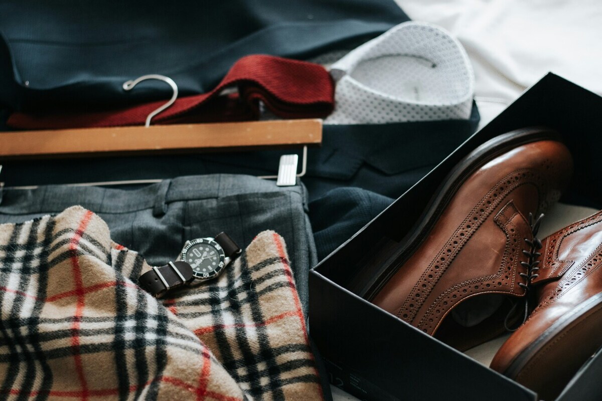 A variety of clothes laid out, including a suit jacket and tie, a pair of pants, a watch, and a pair of shoes.