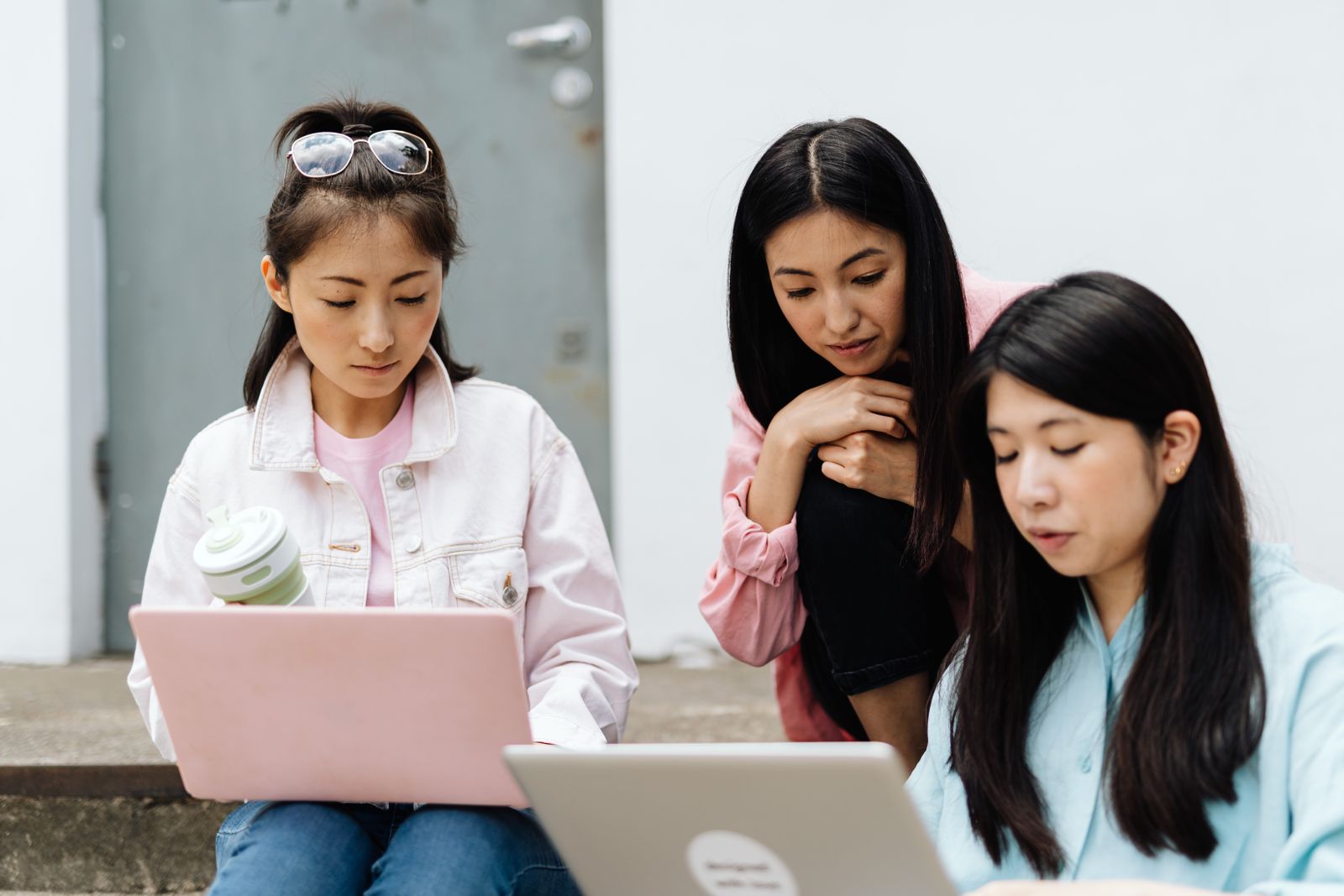 Three university students sitting on campus steps comparing courses on their laptops