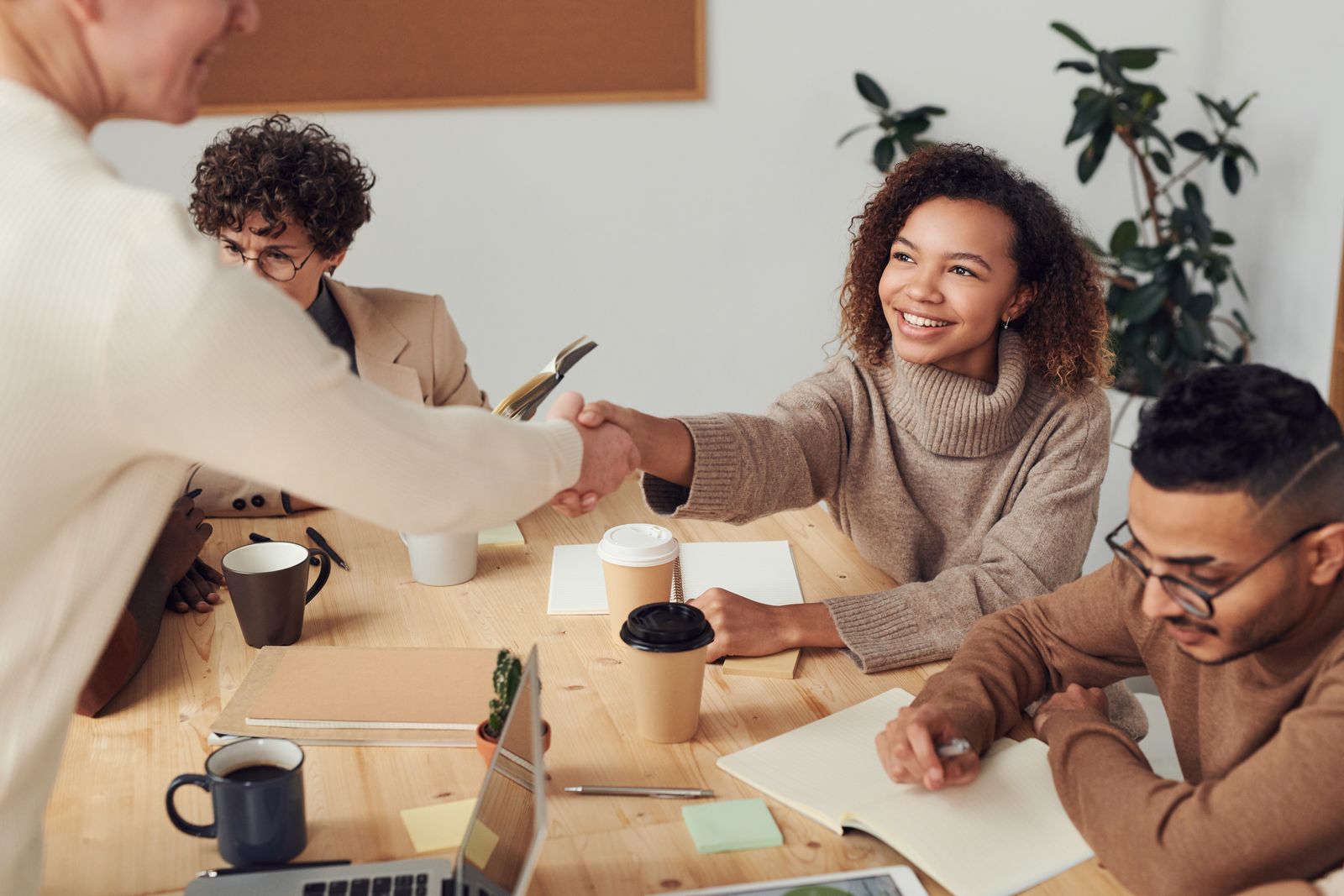 Colleagues shaking hands across a table during a meeting in a bright office