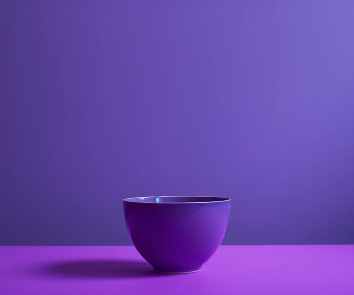A plain purple ceramic bowl placed on a purple surface with a purple gradient background.