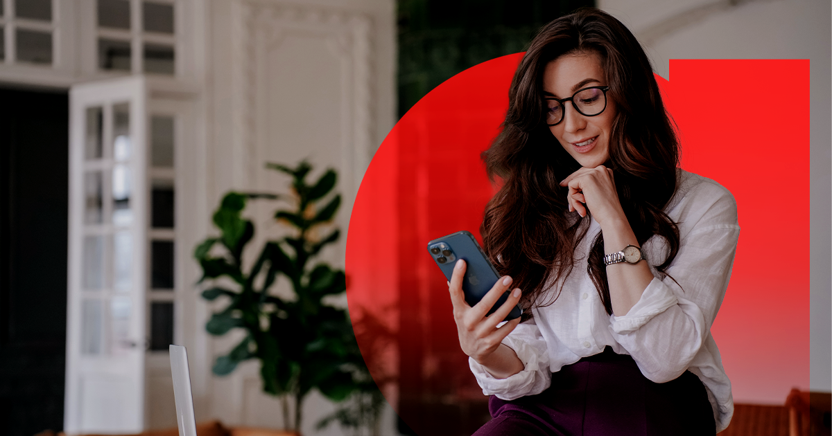 Smiling woman wearing glasses and a white shirt looking at her smartphone, with a red abstract shape and indoor plant in the background.