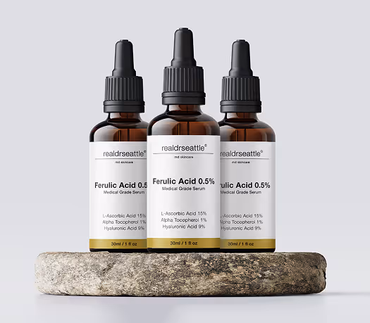 Three amber dropper bottles of realdrseattle Ferulic Acid 0.5% serum displayed on a stone platform.