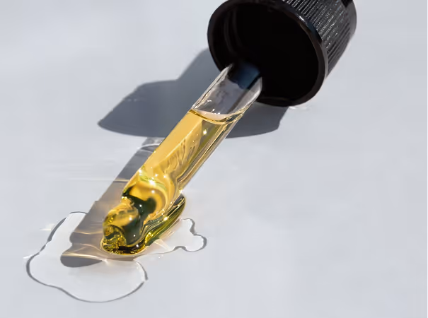 Close-up of a dropper releasing yellow liquid onto a white surface.