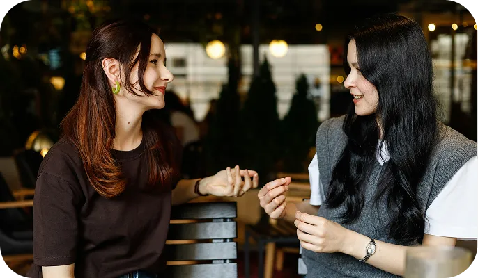 Two young women sitting and talking to each other in a cozy indoor cafe.