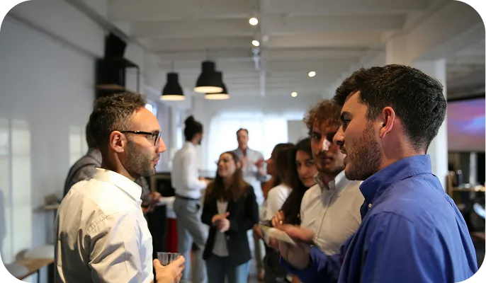 Group of young professionals conversing at a casual indoor networking event or office gathering.