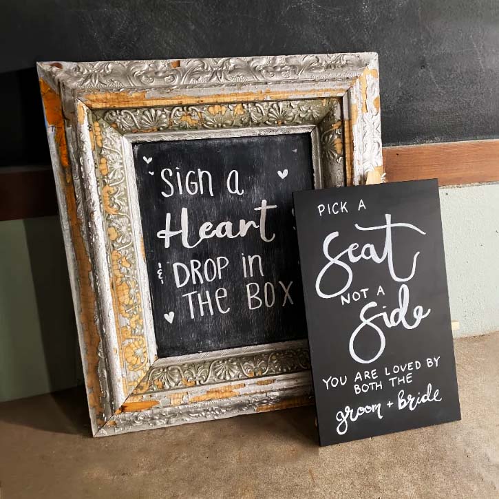 Two chalkboard signs for a wedding: "Sign a heart and drop in the box" and "Pick a seat, not a side"