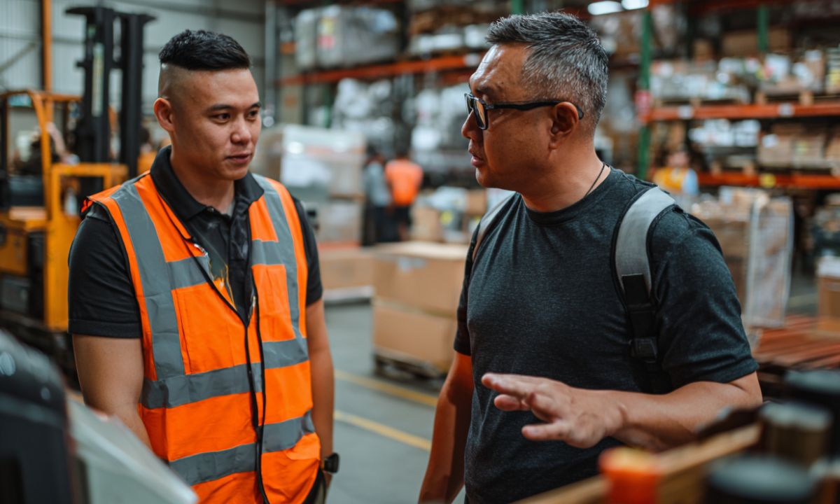 Worker in hi-vis talking with a colleague in a warehouse, illustrating safety communication across language barriers