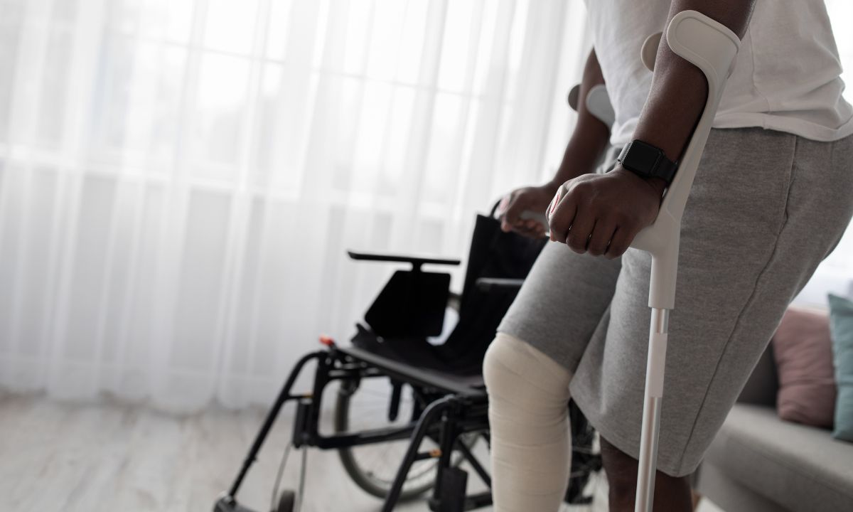 Person on crutches with a leg bandage standing beside a wheelchair, illustrating recovery and return to work after injury