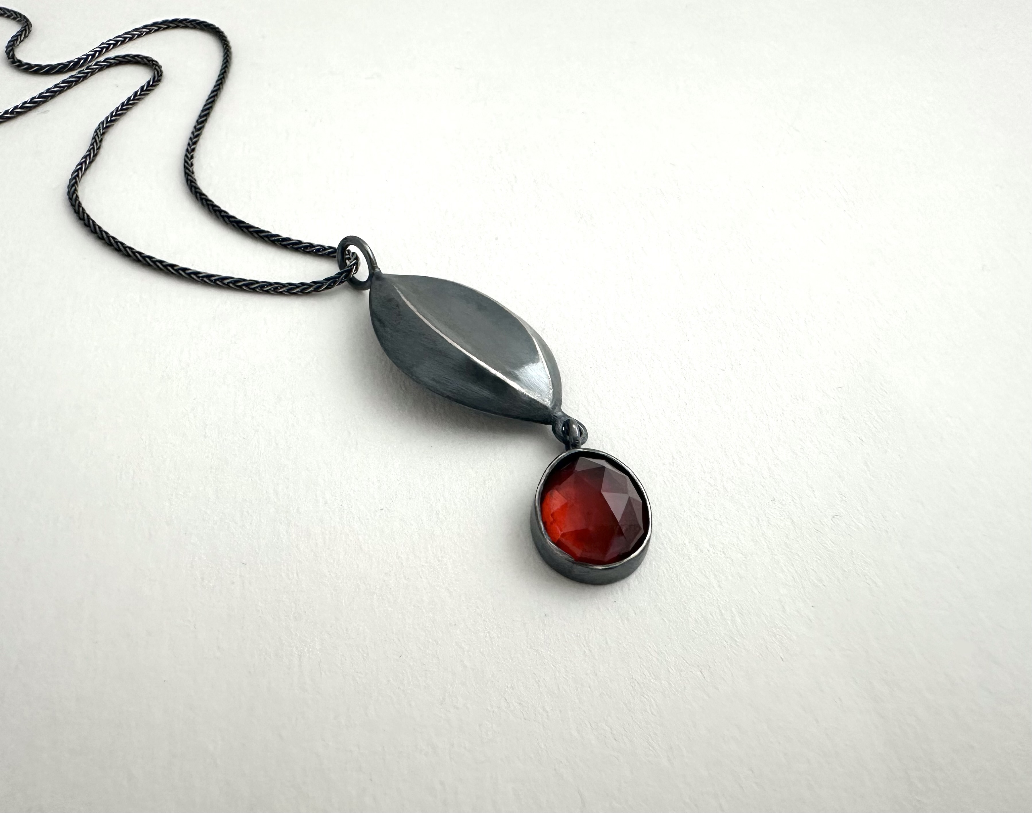 Melon Necklace with Garnet, 2025 | Cast and fabricated oxidized sterling silver, hessonite garnet; pendant is 2 x ¾ inches, 16 inch sterling silver wheat chain