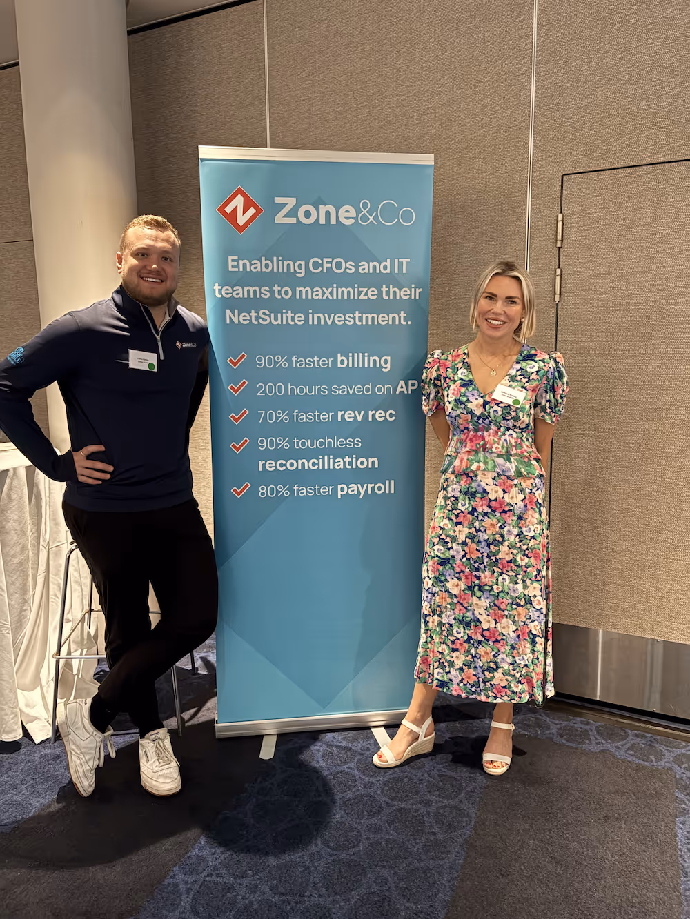 Man and woman standing beside a Zone&Co banner listing benefits like faster billing, 200 hours saved on AP, and touchless reconciliation.