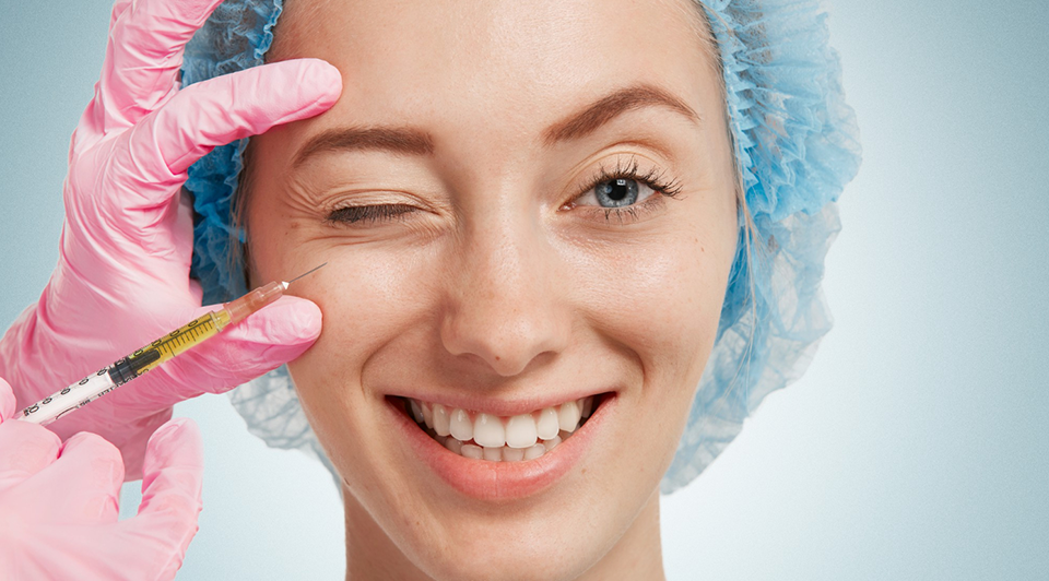 Young woman wearing medical headwear while doctor injects her face