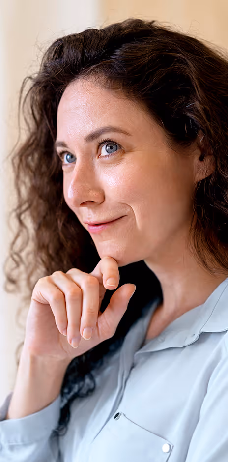 Thoughtful woman with curly brown hair resting her chin on her hand, looking slightly upward.