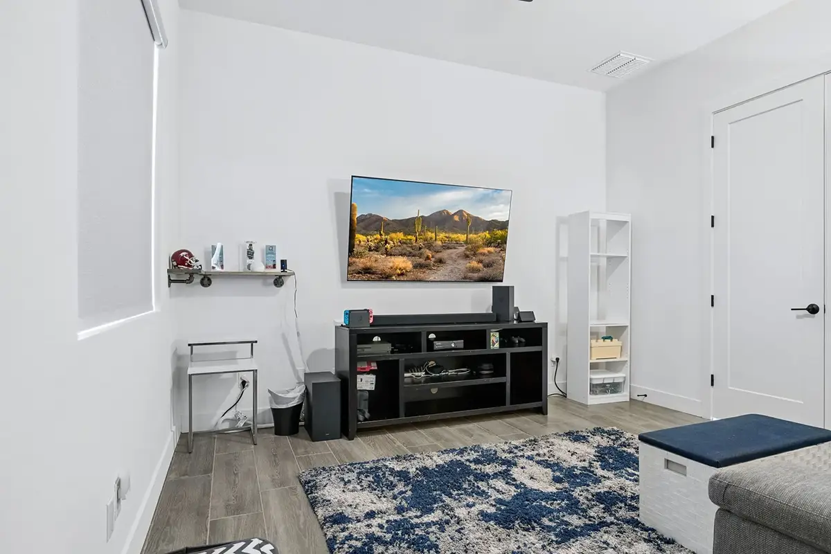 Bonus room with wall-mounted TV, media console, gaming setup, blue shag rug, white walls, and wood-look tile flooring