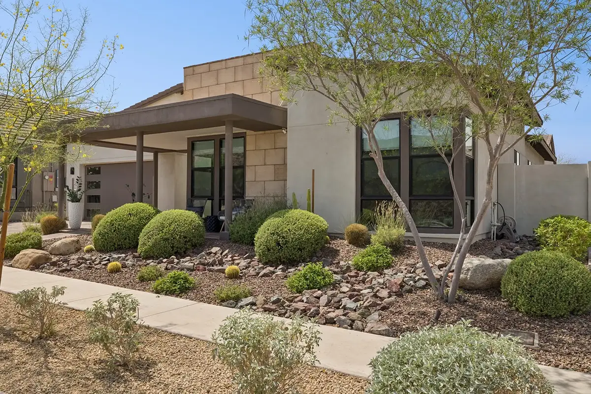 Front exterior of modern desert home with stone facade, covered entry, floor-to-ceiling windows, and xeriscaped front yard