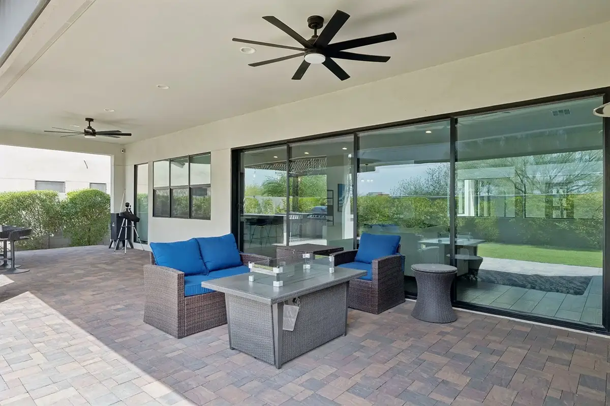Covered patio with wicker seating, blue cushions, fire pit table, large ceiling fan, and sliding glass doors to the interior