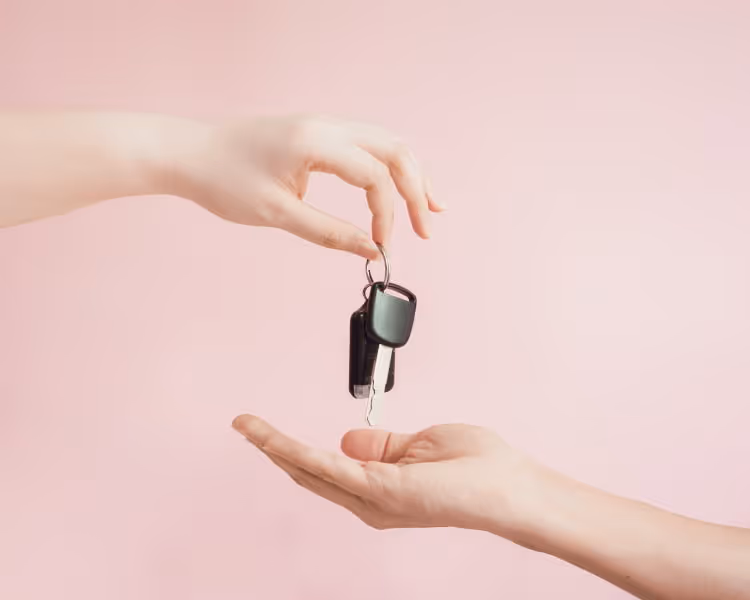 Two hands exchanging car keys on a pink background
