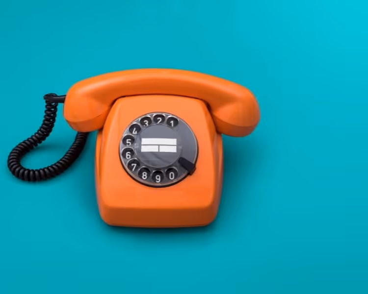 Orange retro rotary phone on a teal background