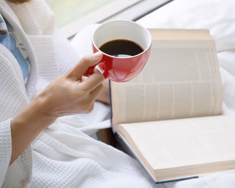 A woman in a robe holding a cup of coffee and a book