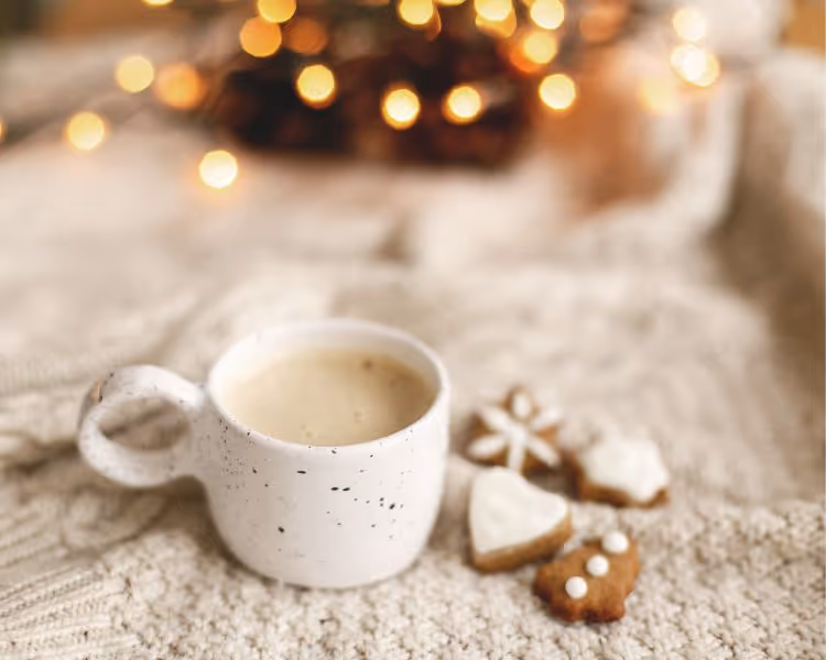 Cafe latte in a white ceramic mug on a white blanket with cookies