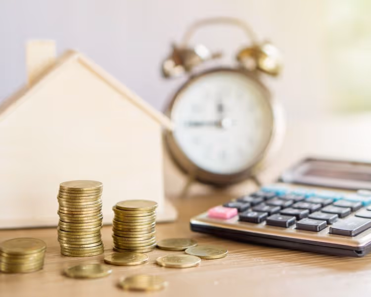 Coins, clock, calculator, toy wood house on table