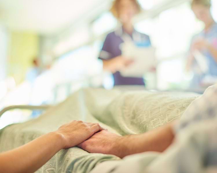 adult child holding a senior's hand in hospital