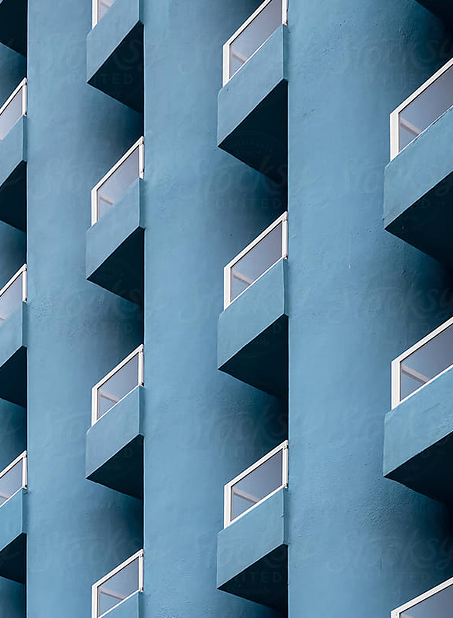 Façade d'un bâtiment bleu avec des balcons symétriques équipés de garde-corps en verre.