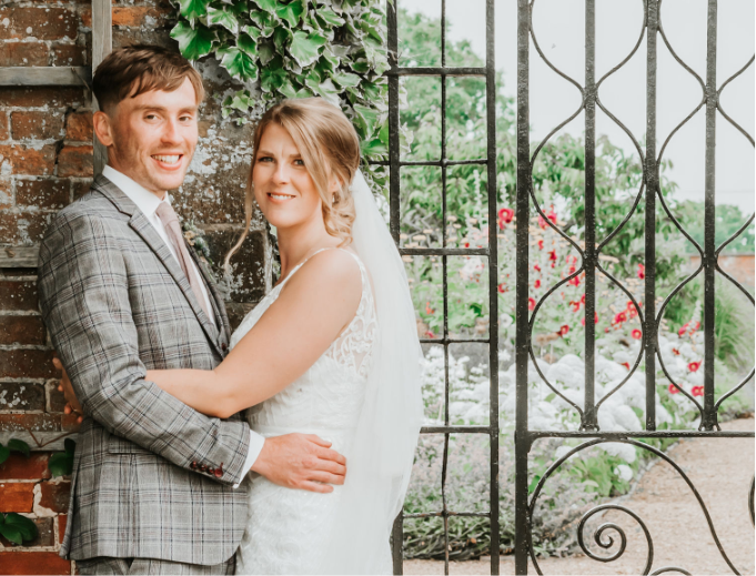 A newly wed couple standing in front of the elegant gate of their wedding venue. Gemma Randall Photography ©