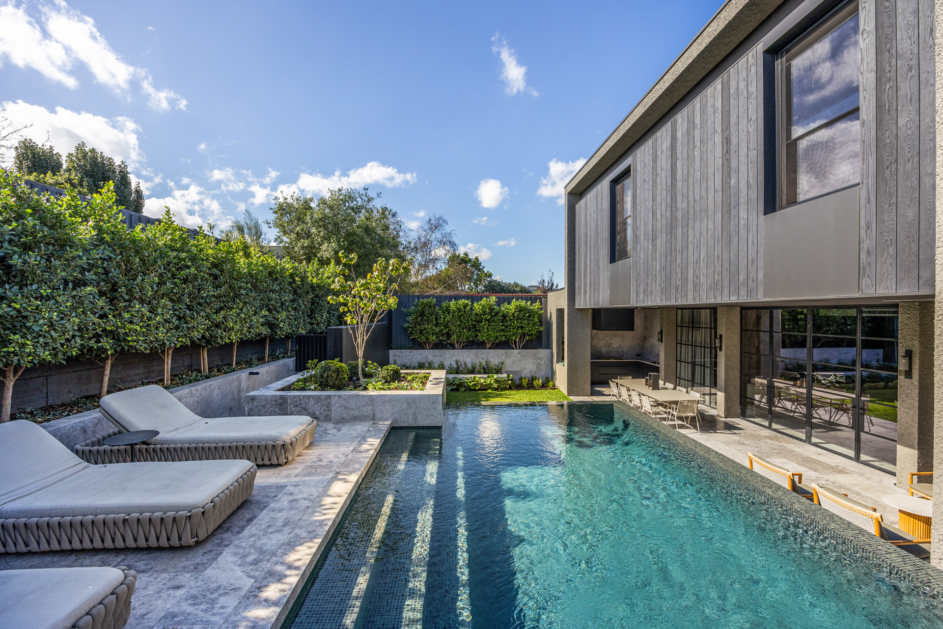 Luxury backyard with pool, garden, and alfresco dining area in a modern Melbourne home by BG Construction, featuring natural stone finishes and contemporary facade design.
