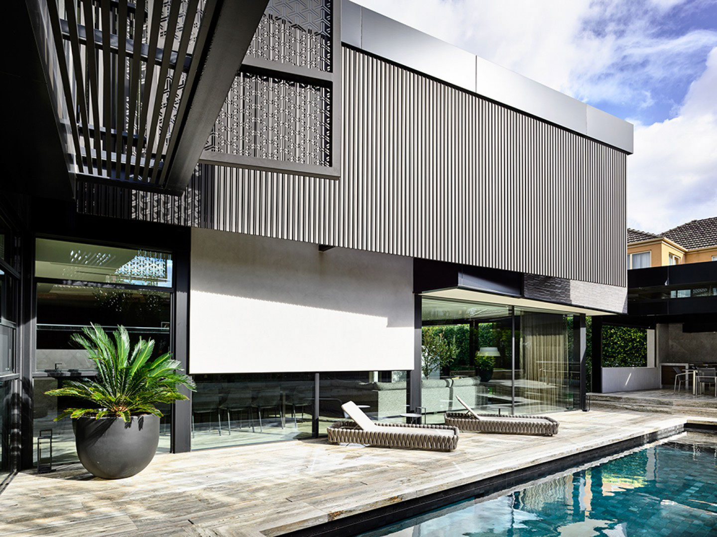Contemporary Melbourne home with custom aluminium cladding and poolside retreat by BG Construction, featuring vertical panelling, sun loungers, and expansive glass doors.