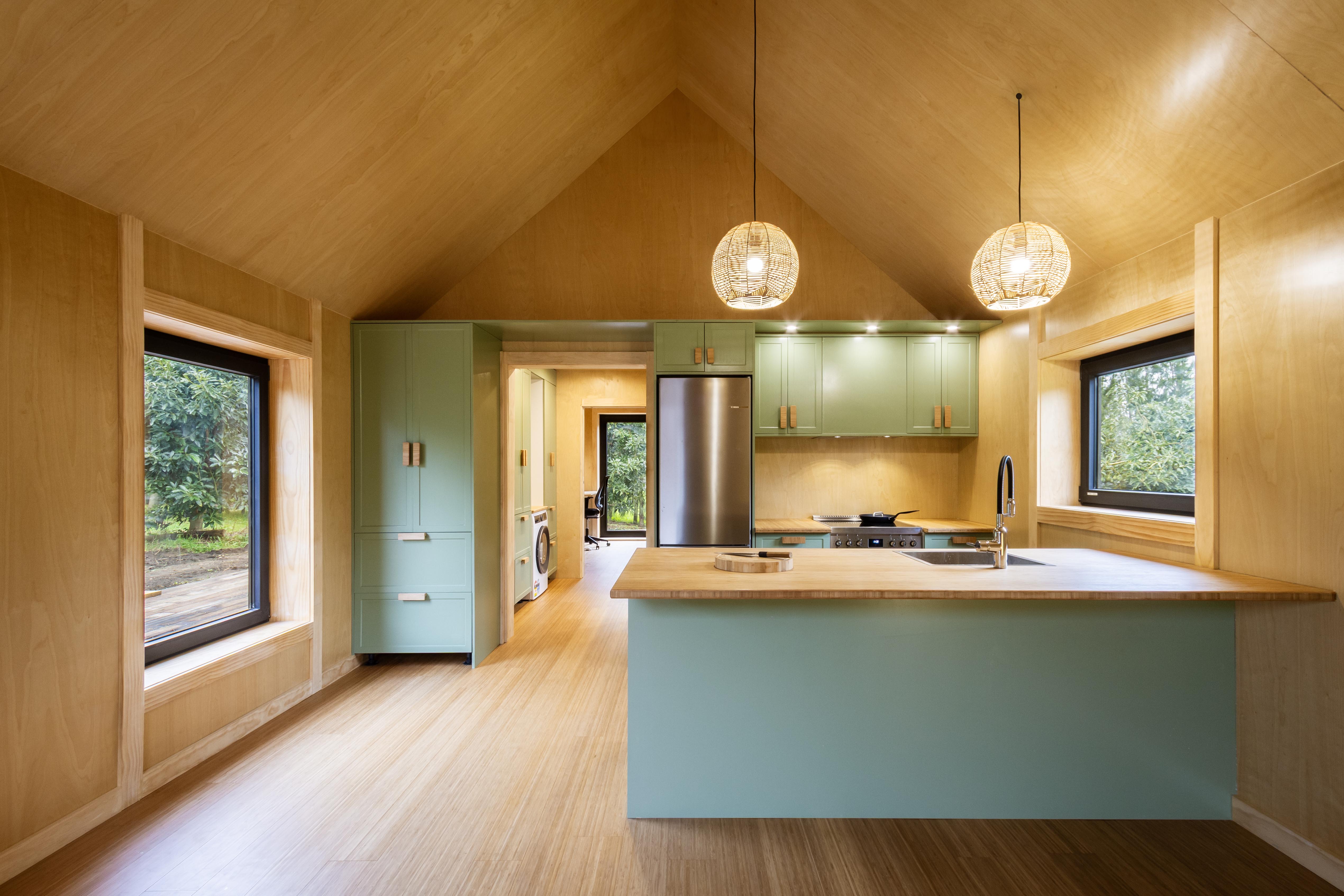The interior of a new kitchen showing worktops, light green cupboards and wooden walls and ceiling.