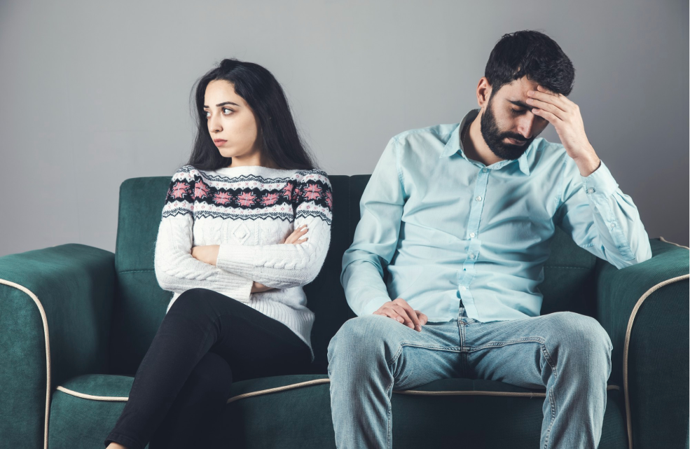Upset couple sitting on couch facing away from each other, symbolizing emotional tension and relationship strain