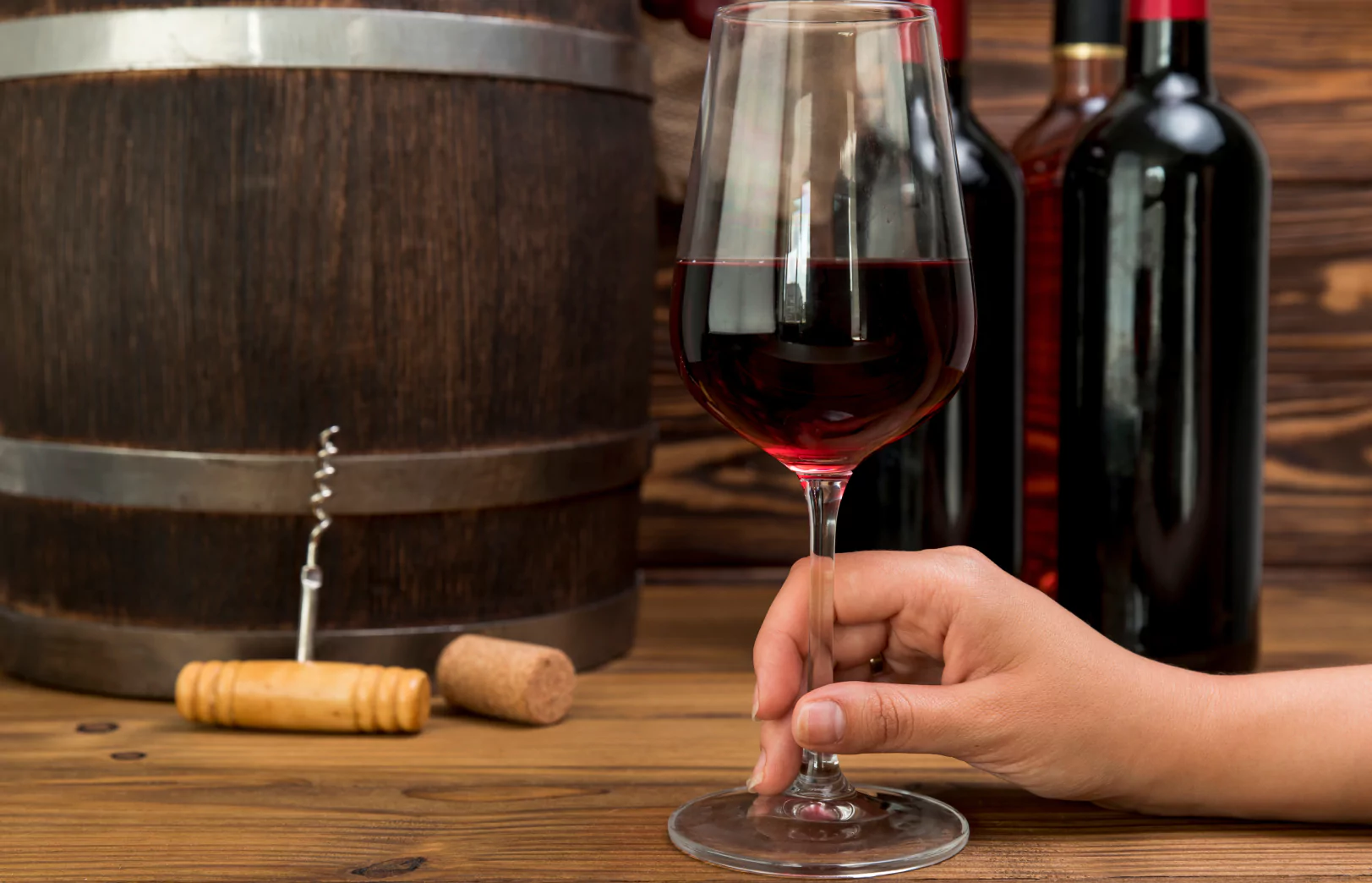 Wine glass held by hand near wooden barrel