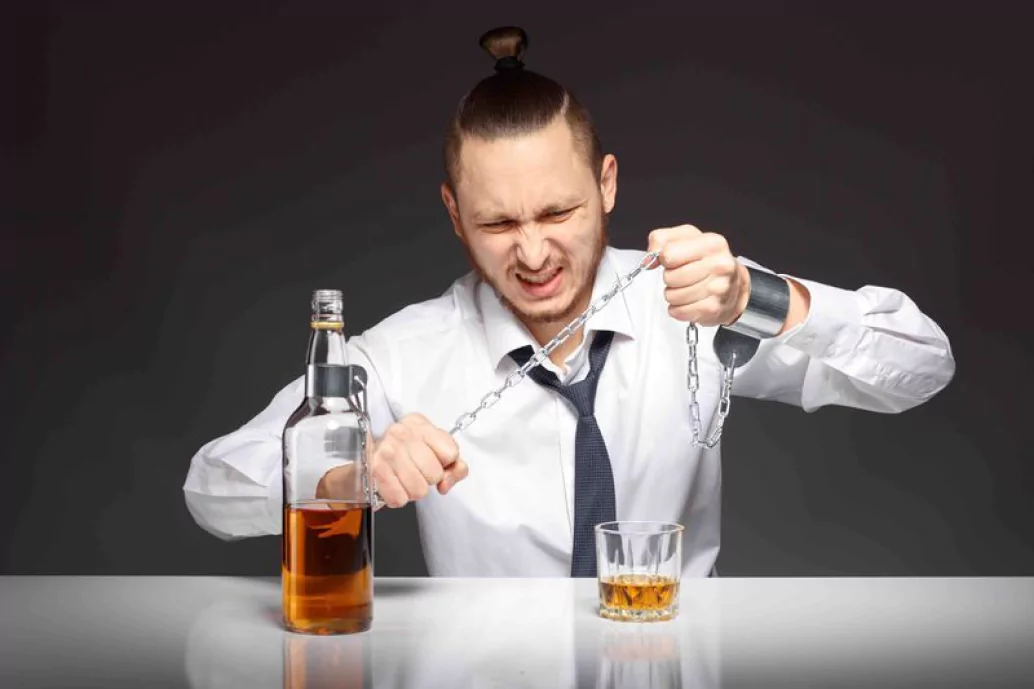 A formally dressed man in a shirt and tie holds a bottle of alcohol