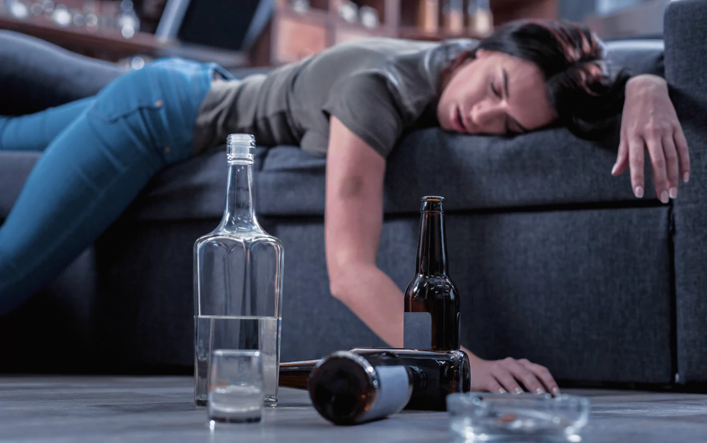 A woman lying on the sofa next to a bottle of alcohol.