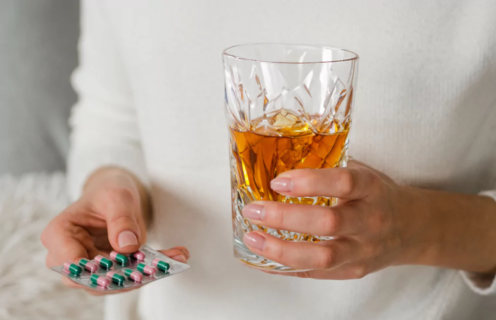 A person holding a glass of alcohol and a pill