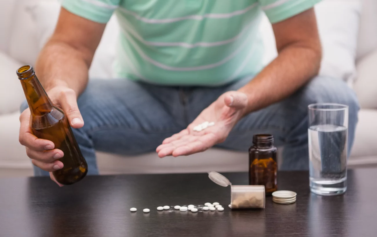 Man holding pills and a bottle of alcohol