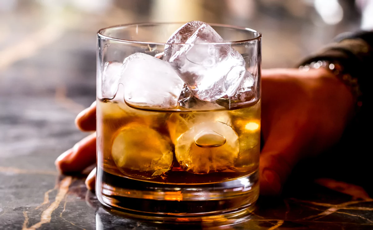 Person holding a glass of whiskey with ice cubes
