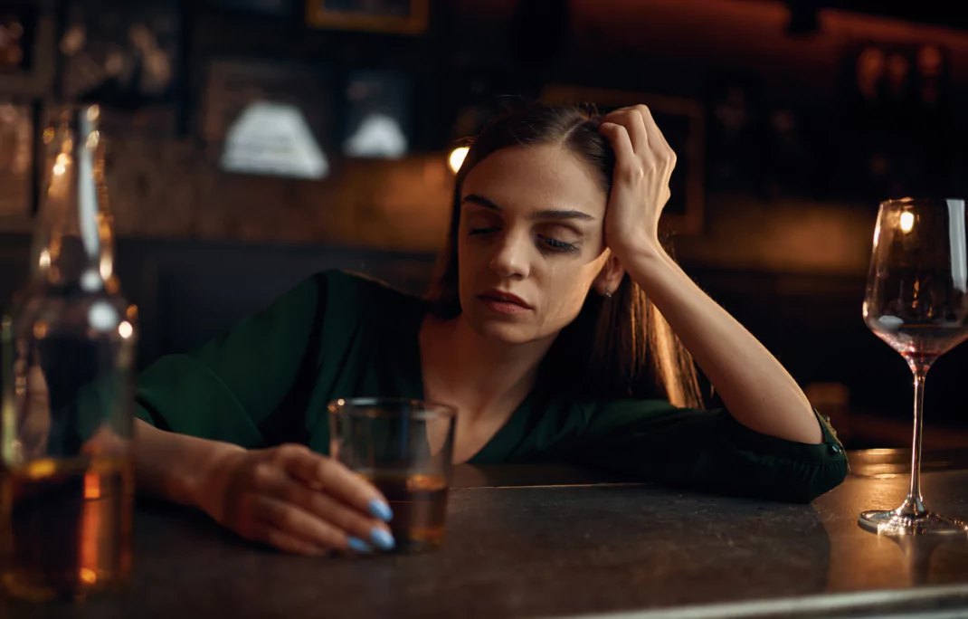 A woman sitting at a bar with a glass of alcohol