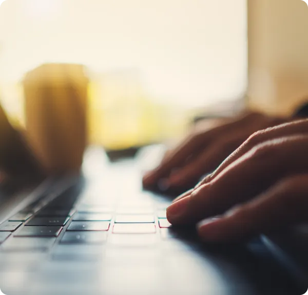 Close-up of hands typing on a laptop keyboard with warm lighting.