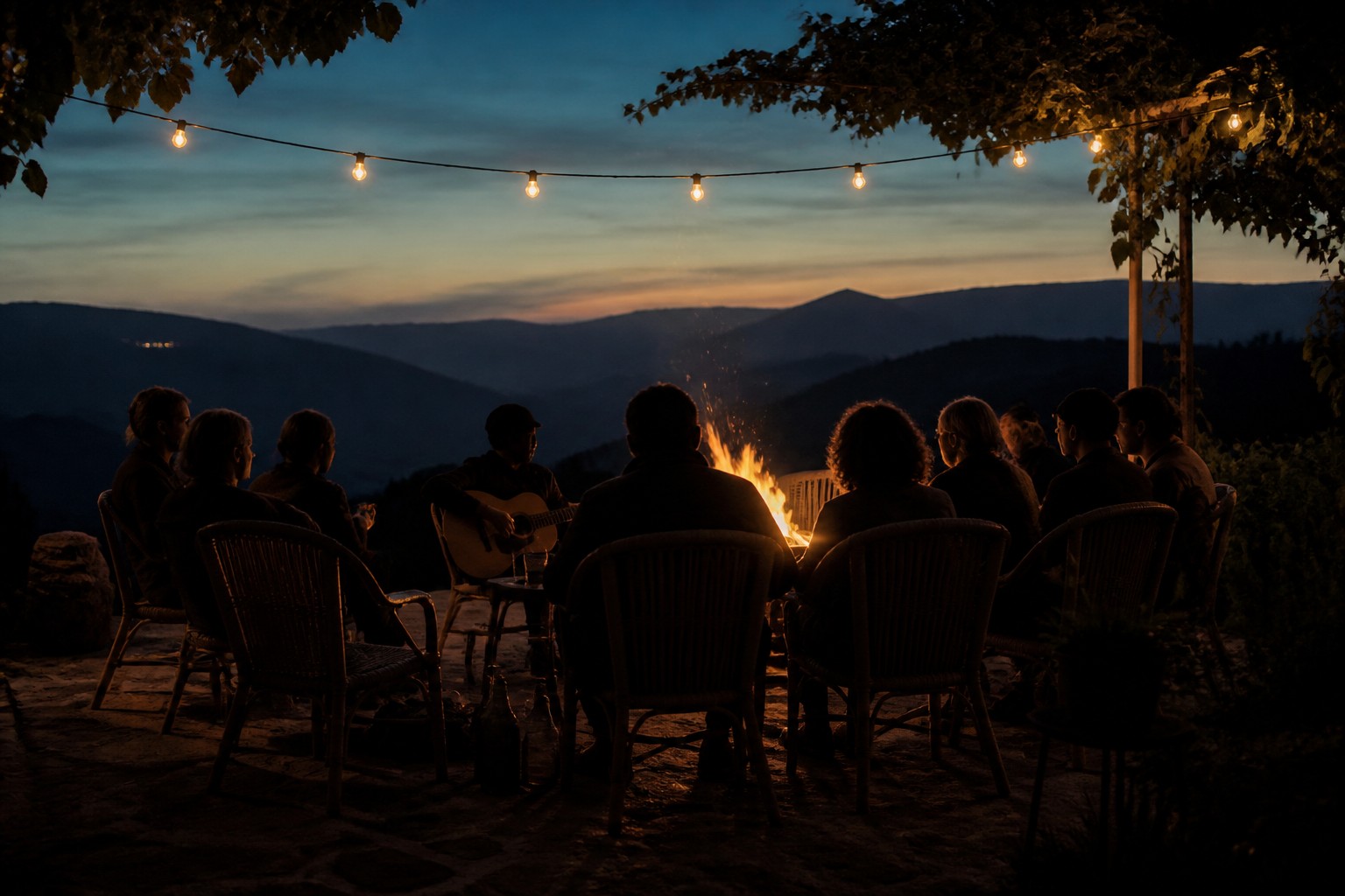Menschen sitzen abends am Lagerfeuer auf einer Terrasse in den Bergen, jemand spielt Gitarre, KI-generiertes Bild