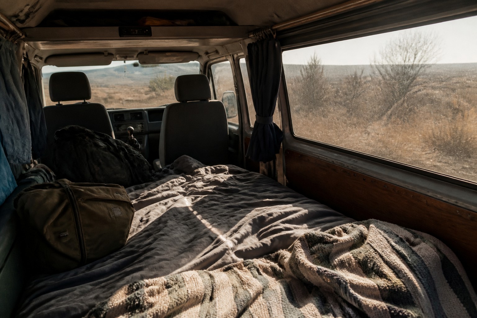 Innenraum eines alten VW-Busses mit umgeklappter Rückbank als Bett, Blick auf die trockene Landschaft Andalusiens, KI-generiertes Bild
