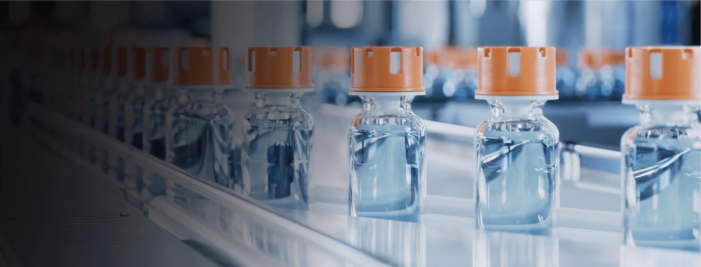 Row of clear glass vials with orange caps on a production line in a pharmaceutical manufacturing setting.