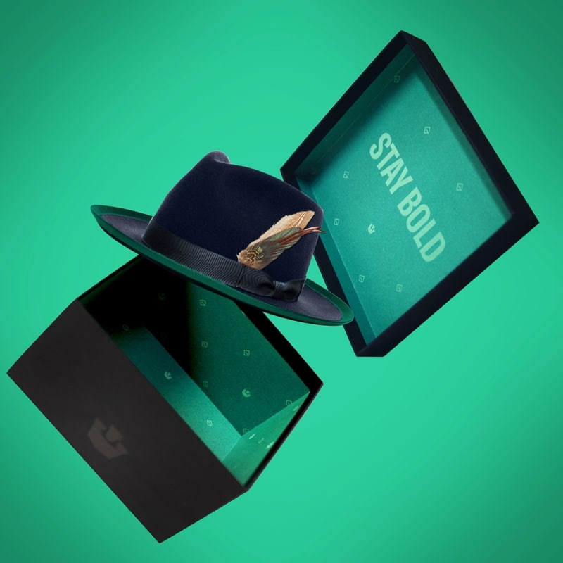 A Goorin Bros. Hat coming out of box in mid air with a green back drop with highlights.