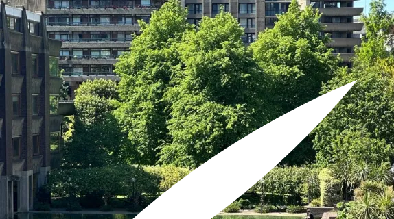 Urban scene with lush green trees in the foreground and modern apartment buildings in the background under a clear sky.