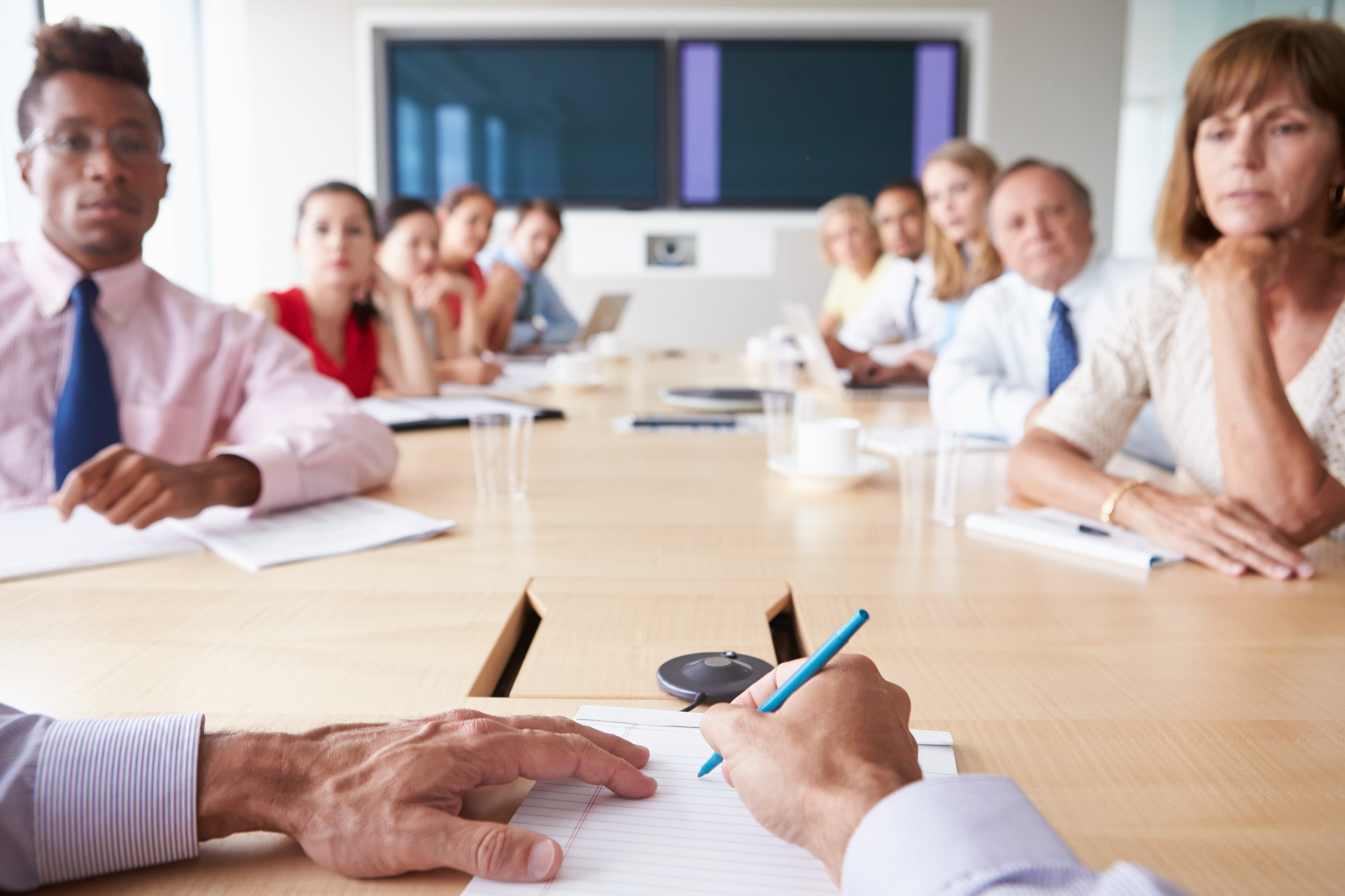 Staff seated around a long conference table during a project meeting, several looking doubtful and unconvinced