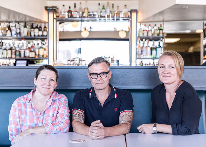 Three people sitting at bar, with liquor bottles in background