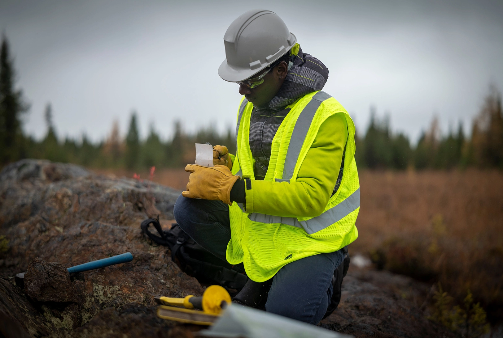 Field technician working in the field with PPE (i.e. hard hat, high-visibility vest, gloves, and safety glasses.