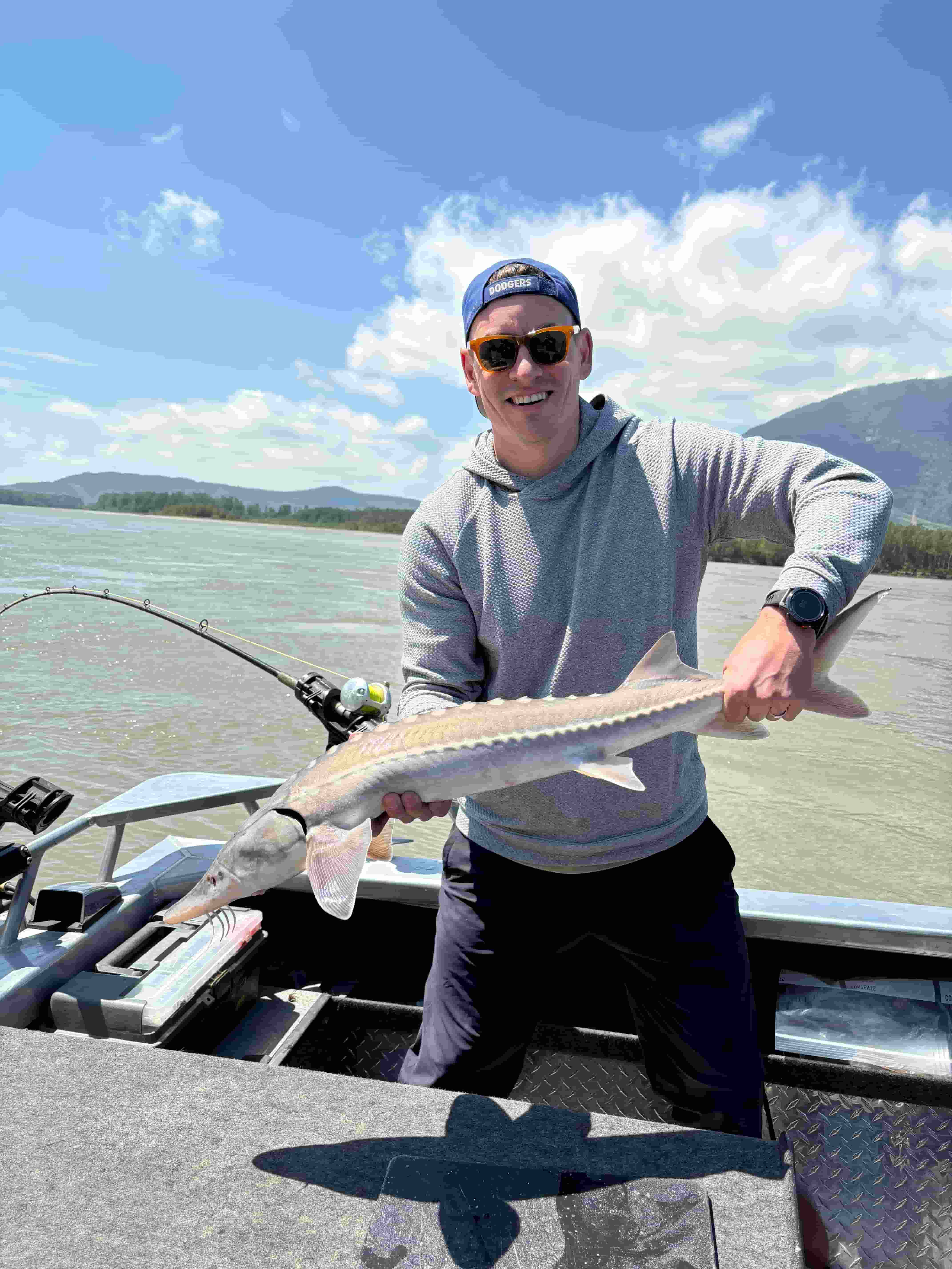 a man holding a small sturgeon in a boat on the river
